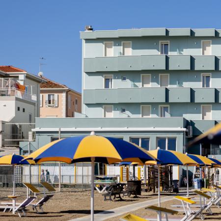 Sunny beach with colorful umbrellas and a hotel in the background.
