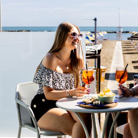 Two smiling friends toast by the sea, enjoying the summer sun.