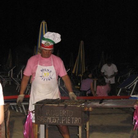 Chef on the beach with grill and chef's hat.