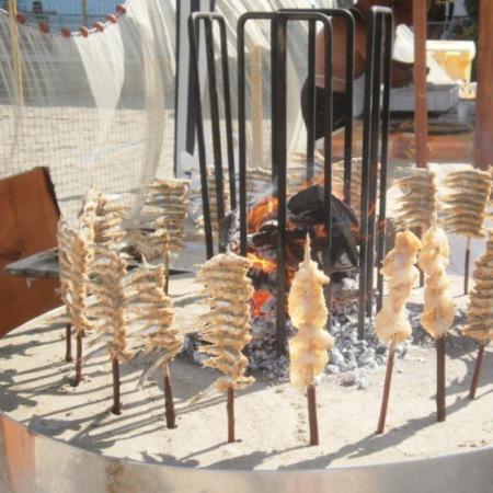 Sardines roasted on skewers around a fire.