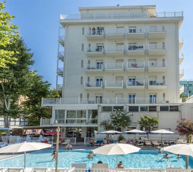 Hotel con piscina all'aperto, ombrelloni e balconi soleggiati.