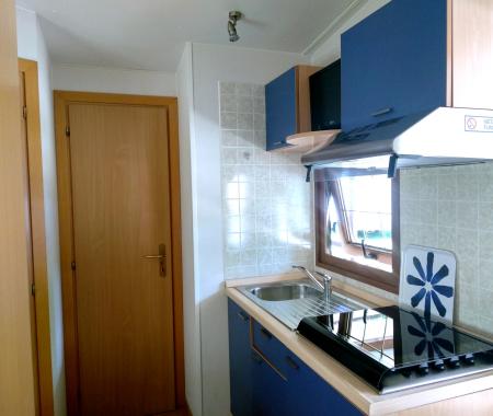 Small kitchen with stove, sink, and hood. Wooden door and window.