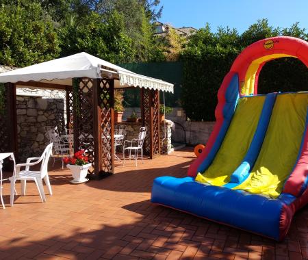 Jardin avec gazebo, tables, chaises et toboggan gonflable coloré.