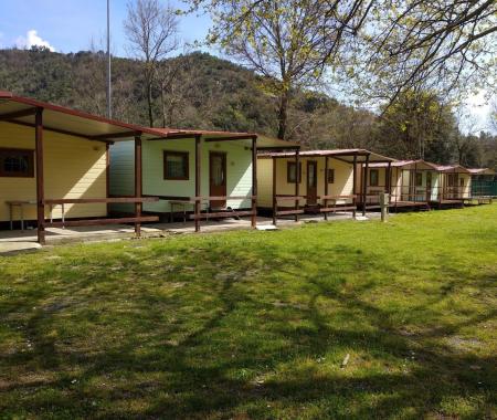 Row of wooden houses on a green lawn with trees and hills.