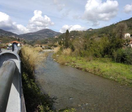 Fluss mit Brücken, grünen Hügeln und verstreuten Häusern unter einem bewölkten Himmel.