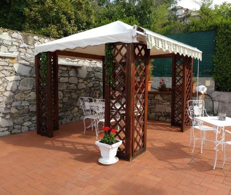 Gazebo avec tables et chaises en fer forgé sur une terrasse en terre cuite.