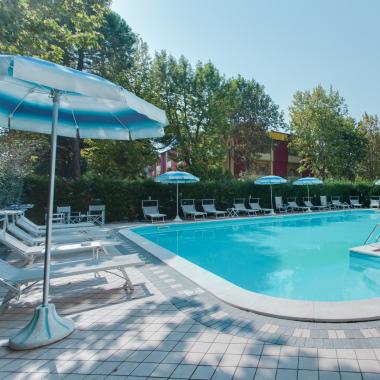 Piscina all'aperto con lettini e ombrelloni, circondata da alberi.