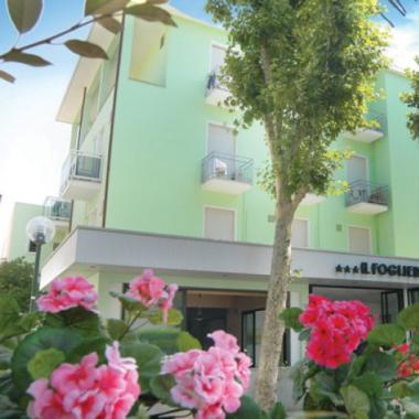 Hotel verde con fiori rosa e alberi intorno.