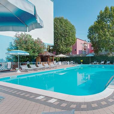 Piscina all'aperto con lettini e ombrelloni, circondata da alberi.