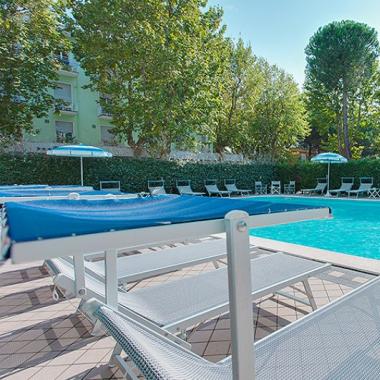 Piscina all'aperto con lettini e ombrelloni, circondata da alberi.