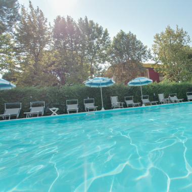 Piscina all'aperto con ombrelloni e lettini, circondata da alberi.