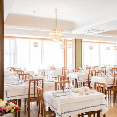 Ristorante elegante con tavoli apparecchiati, lampadari e atmosfera luminosa.