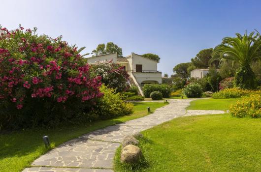 Giardino fiorito con vialetto e casa bianca.