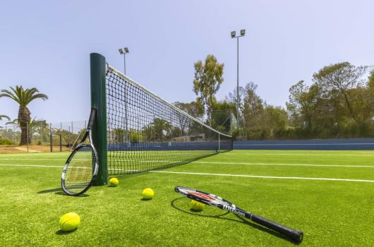 Campo da tennis con racchette e palline su erba sintetica.