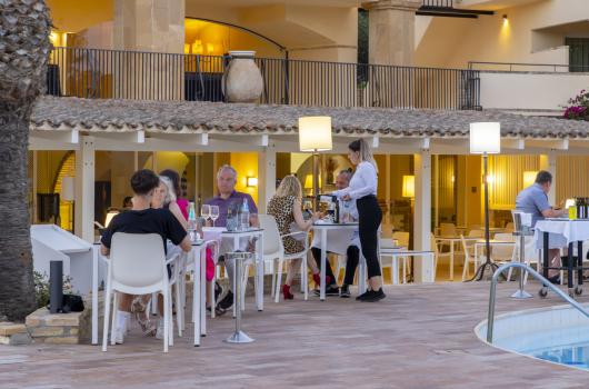 Persone cenano all'aperto vicino a una piscina in un ristorante elegante.