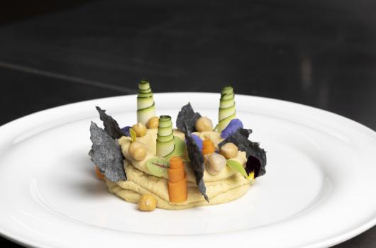 Piatto gourmet con hummus, verdure e decorazioni eleganti.