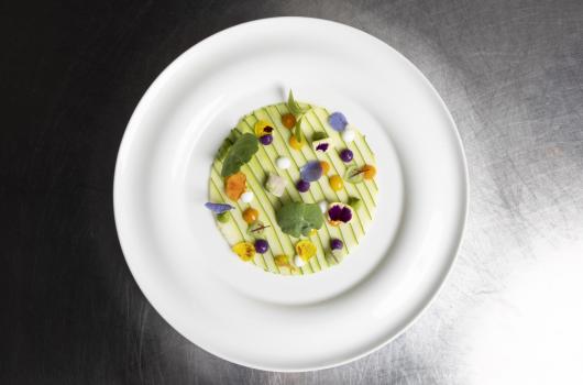 Piatto elegante con fiori commestibili e verdure a fette.