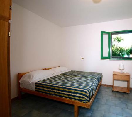 Zimmer mit Doppelbett und Etagenbetten, offenes Fenster.