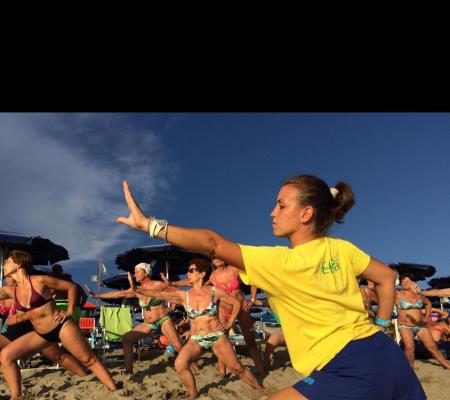 Fitnesskurs am Strand mit Trainerin in gelbem Shirt.