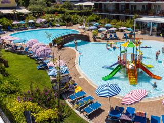 Pool with colorful slides and loungers under striped umbrellas.
