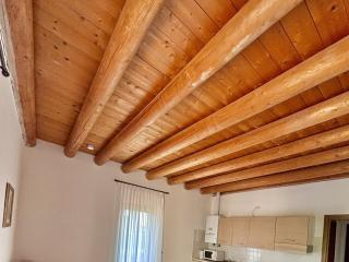 Living room with wooden ceiling, kitchen, and table.