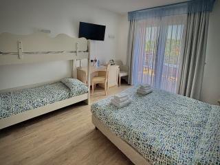 Hotel room with double and bunk beds, TV, desk, and balcony.