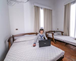 Bambino con laptop in camera da letto con due letti.