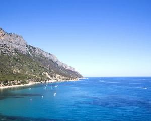 Costa rocciosa con mare blu e barche a vela.