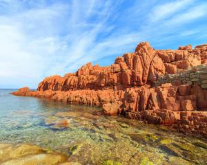 Scogliere rosse e mare cristallino sotto un cielo azzurro.