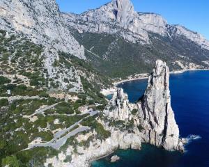 Scogliera imponente su mare blu, circondata da montagne.