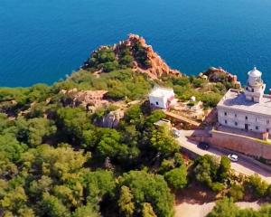 Faro su scogliera con vista mare e vegetazione rigogliosa.