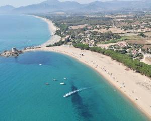 Spiaggia sabbiosa con mare cristallino e paesaggio collinare sullo sfondo.