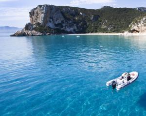 Gommone su acque cristalline vicino a una spiaggia con grotte.