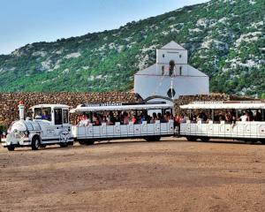 Trenino turistico bianco davanti a una chiesa e colline verdi.