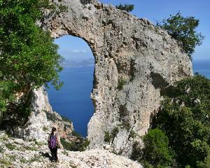 Arco naturale su scogliera con vista mare, escursionista in primo piano.