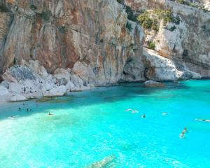 Spiaggia rocciosa con acqua cristallina e bagnanti.