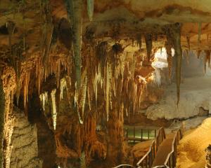 Caverna con stalattiti e stalagmiti illuminate, passerella visibile.