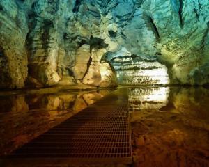 Grotta illuminata con passerella e riflessi sull'acqua.