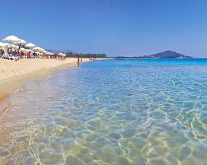 Spiaggia sabbiosa con mare cristallino e ombrelloni bianchi.