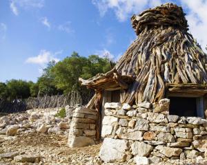 Capanna rustica in pietra e legno in un paesaggio naturale.