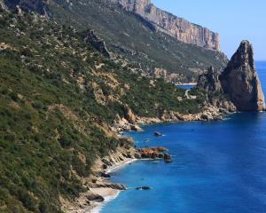 Scogliera rocciosa con mare blu e paesaggio montuoso.