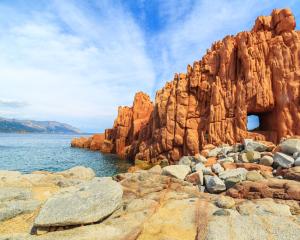 Scogliere rosse a picco sul mare con cielo azzurro.