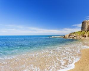 Spiaggia sabbiosa con torre antica e mare cristallino sotto cielo blu.