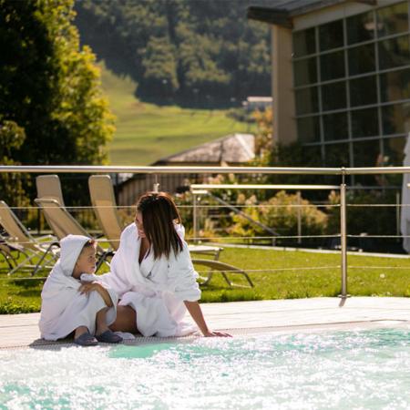 Madre e figlio rilassati a bordo piscina in accappatoio.