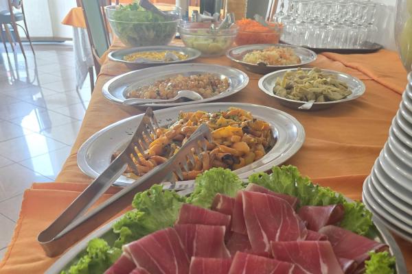 Buffet con affettati e piatti di verdure su tovaglia arancione.