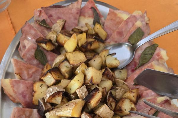 Patate arrosto e prosciutto con salvia su un piatto.