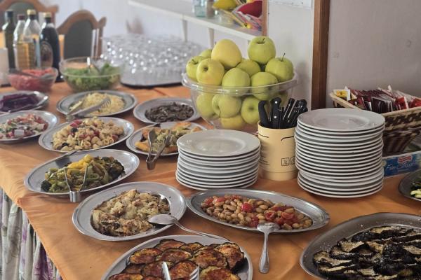 Buffet con piatti vari, frutta e stoviglie su tovaglia arancione.