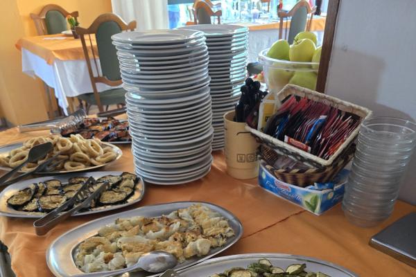 Buffet con pizza, verdure grigliate e piatti impilati.