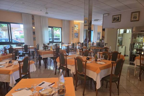 Ristorante accogliente, tavoli apparecchiati con tovaglie arancioni, atmosfera calda e luminosa.