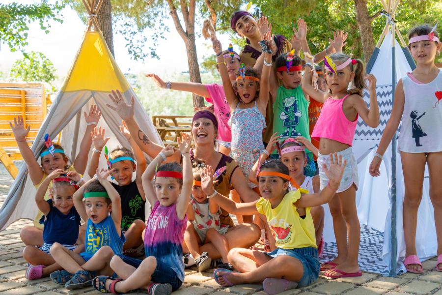 Glückliche Kinder mit bunten Stirnbändern, lächelnd und Hände in der Luft.